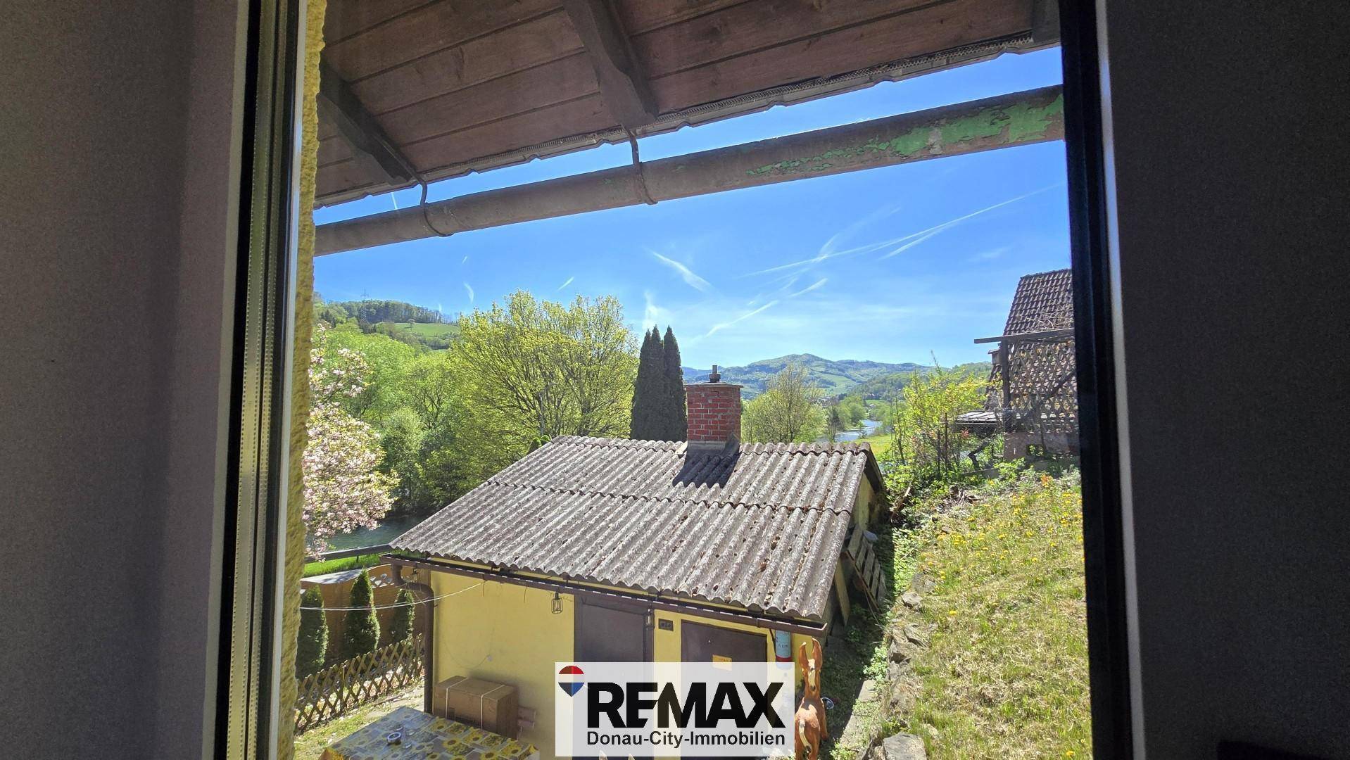 Fensterblick auf ein Nebengebäude und die umliegende grüne Landschaft.