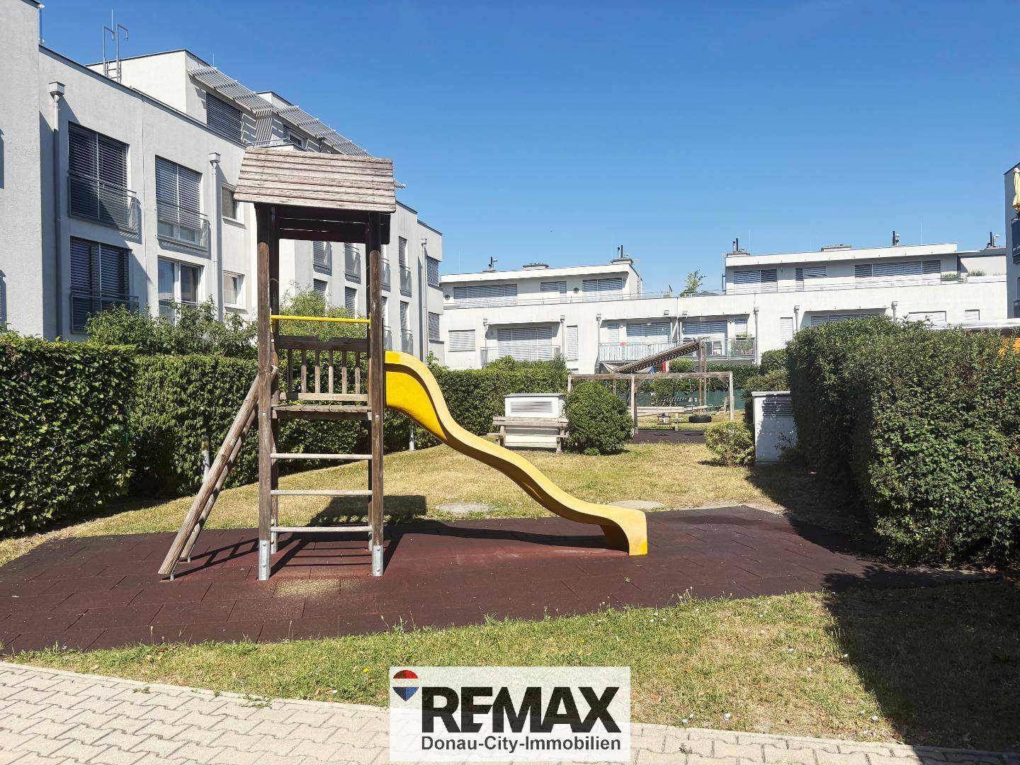 Kinderspielplatz mit gelber Rutsche und Klettergerüst in einer grünen Wohnanlage.