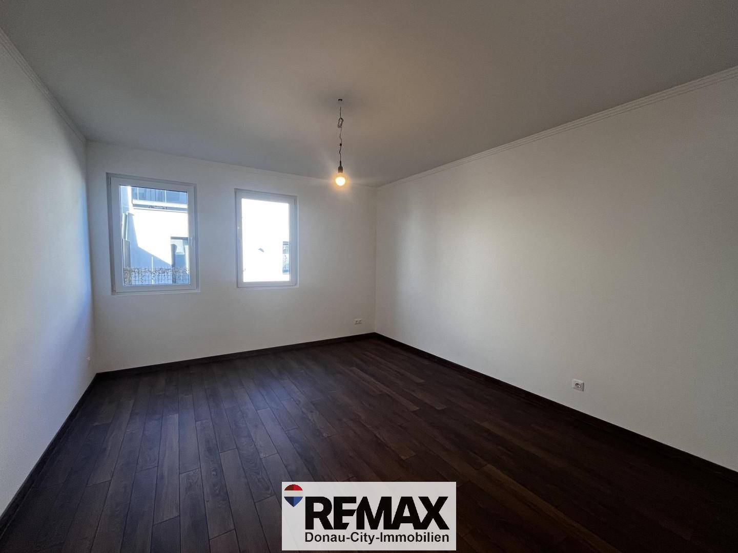Geräumiges Zimmer mit zwei Fenstern und dunklem Holzboden, ideal als Schlaf- oder Arbeitszimmer.