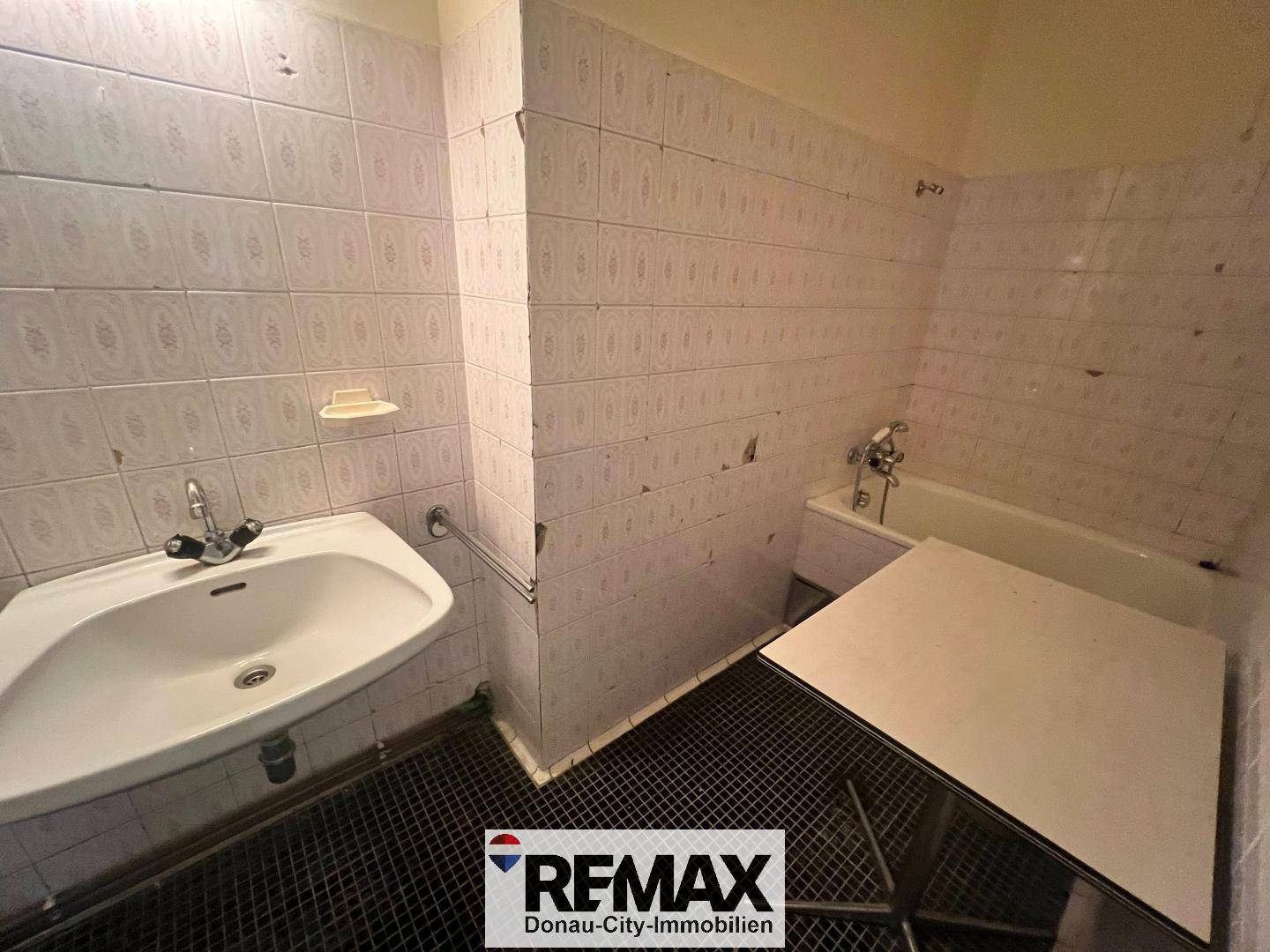 Einfaches Badezimmer mit Waschbecken, Badewanne und weißen Fliesen, renovierungsbedürftig.