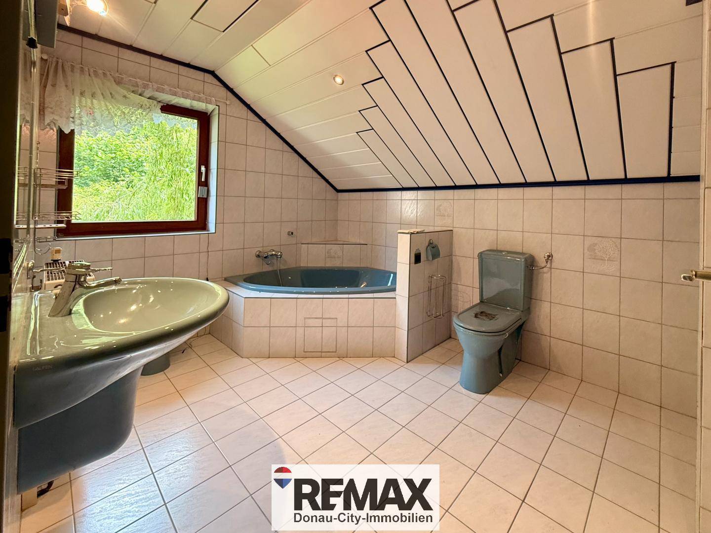 Badezimmer im Dachgeschoss mit hellblauen Fliesen, Eckbadewanne und Fenster.