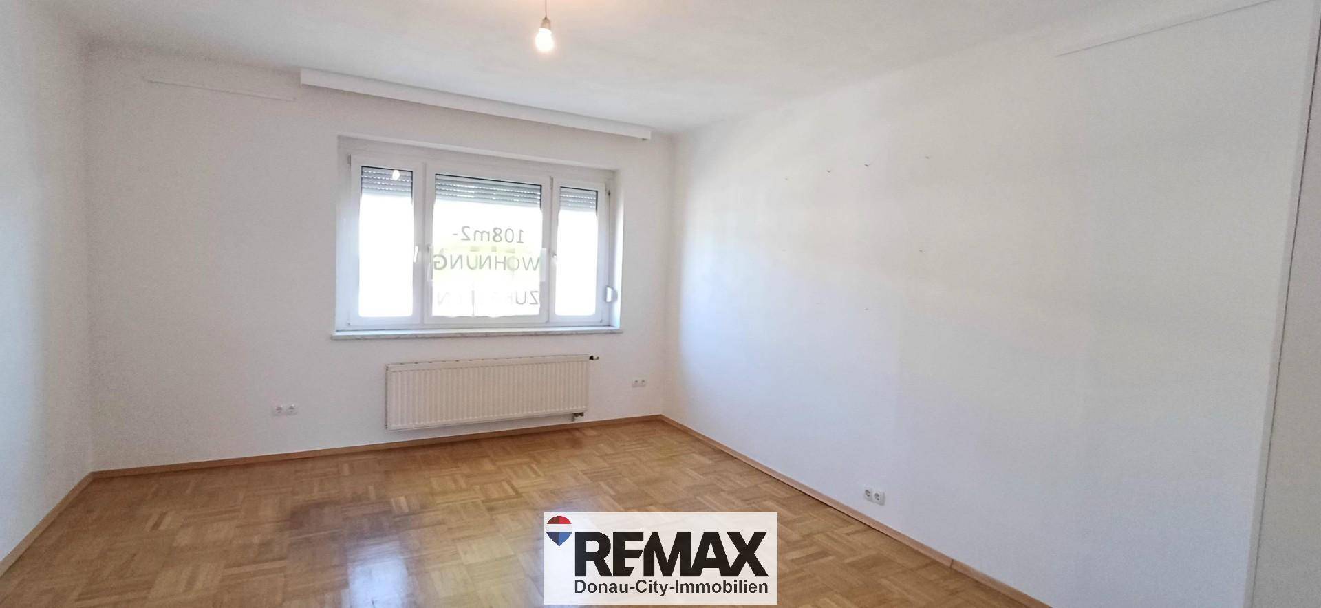 Heller Raum mit Parkettboden, großem Fenster und Heizkörper unter der Fensterbank.