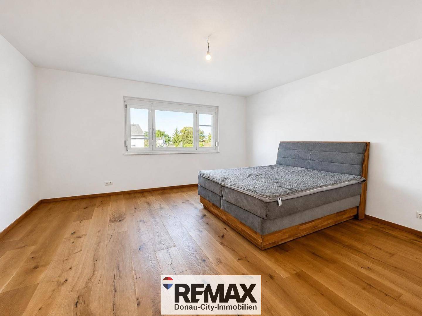 Geräumiges Schlafzimmer mit großem Bett, Holzboden und viel natürlichem Licht durch das Fenster.