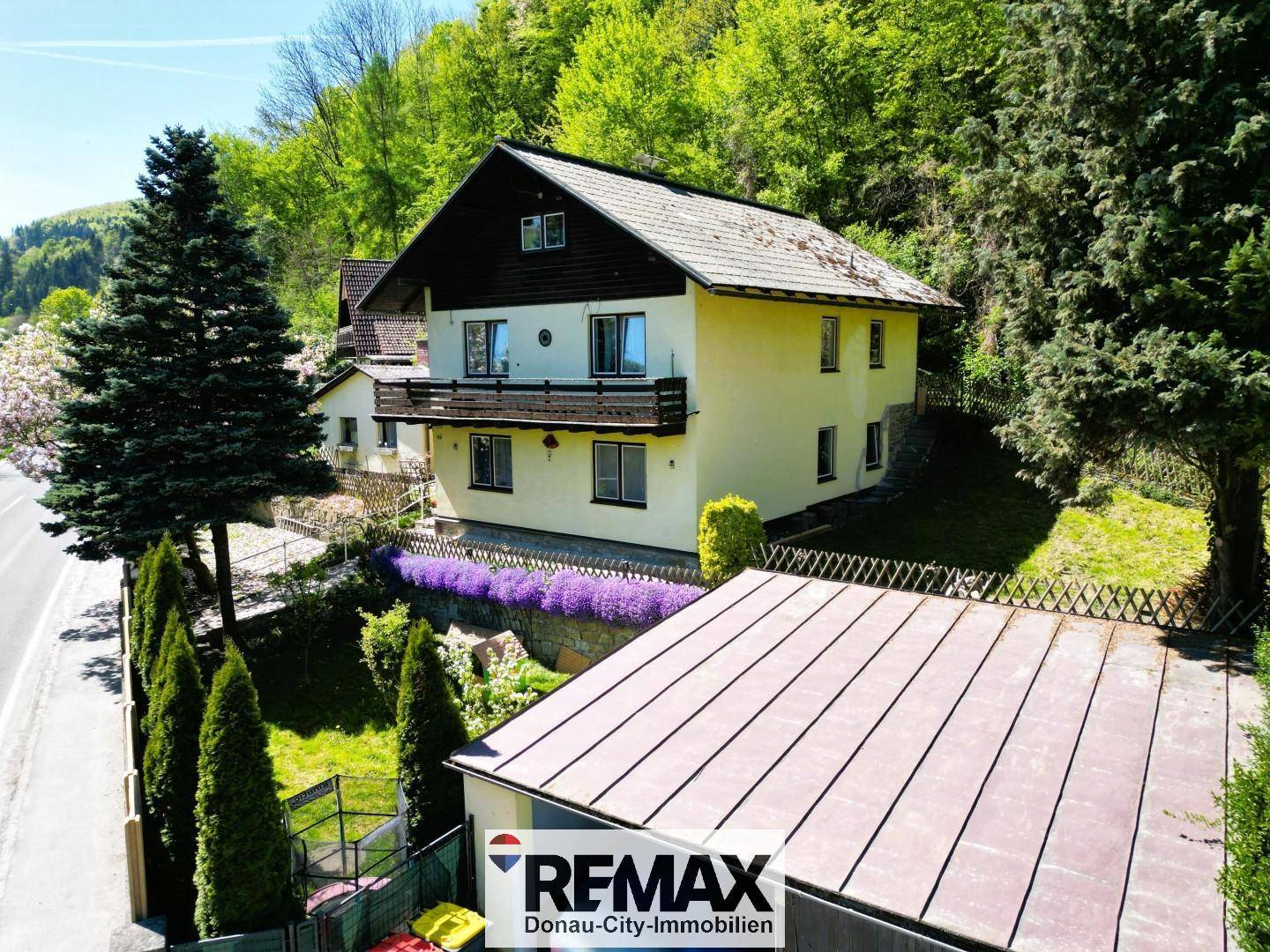 Luftaufnahme eines Einfamilienhauses mit Balkon, umgeben von üppigem Grün und Bäumen.