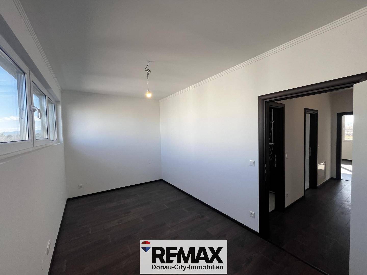 Helles Zimmer mit dunklem Holzboden und breitem Fensterband, ideal als Schlafzimmer.