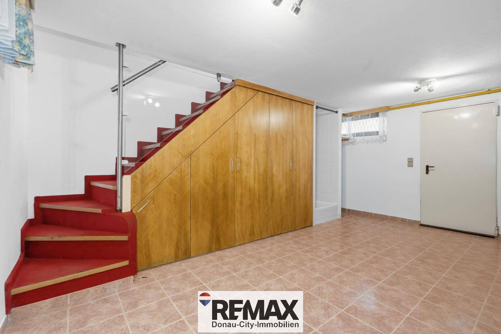 Geräumiger Kellerraum mit Holzschränken unter der Treppe und Fliesenboden.