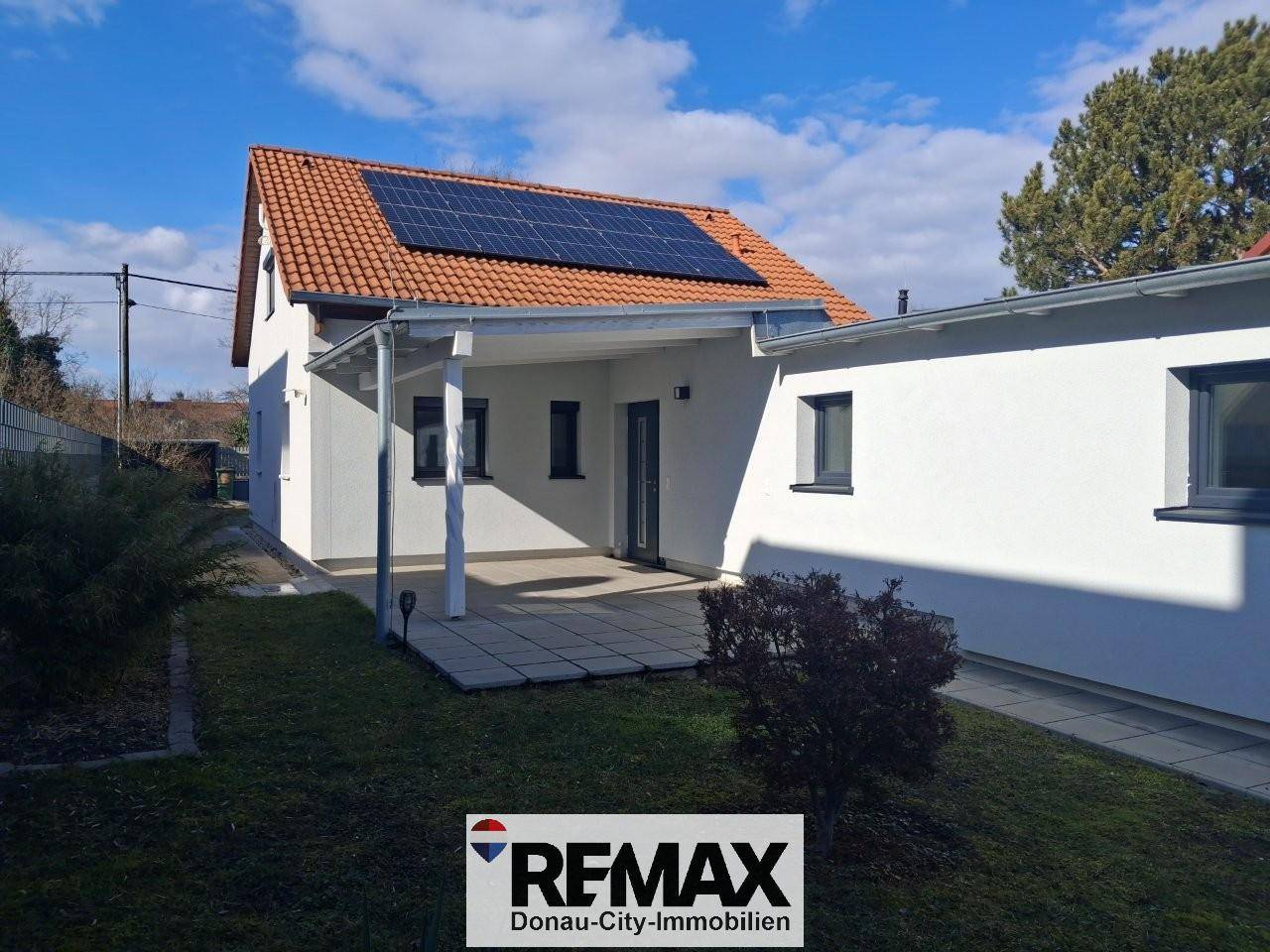 Rückansicht des Hauses mit Solaranlage, überdachter Terrasse und weitläufigem Rasenbereich.