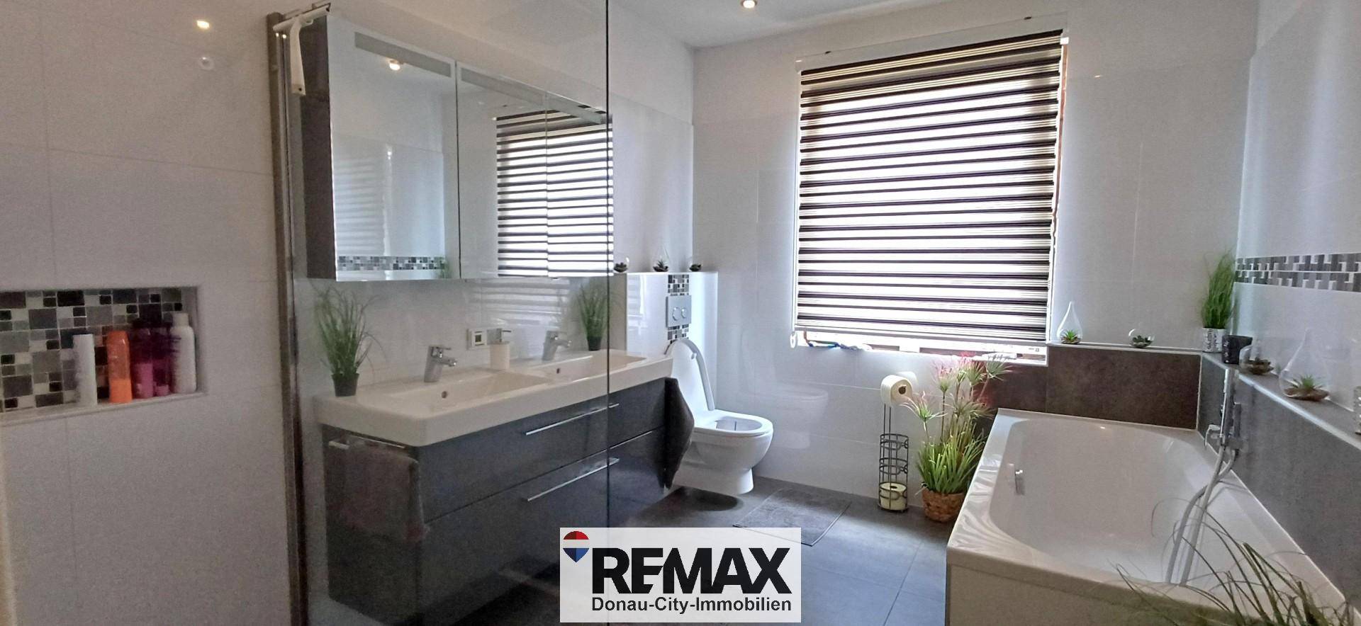 Modernes Badezimmer mit Badewanne, Doppelwaschbecken und Fenster für Tageslicht.