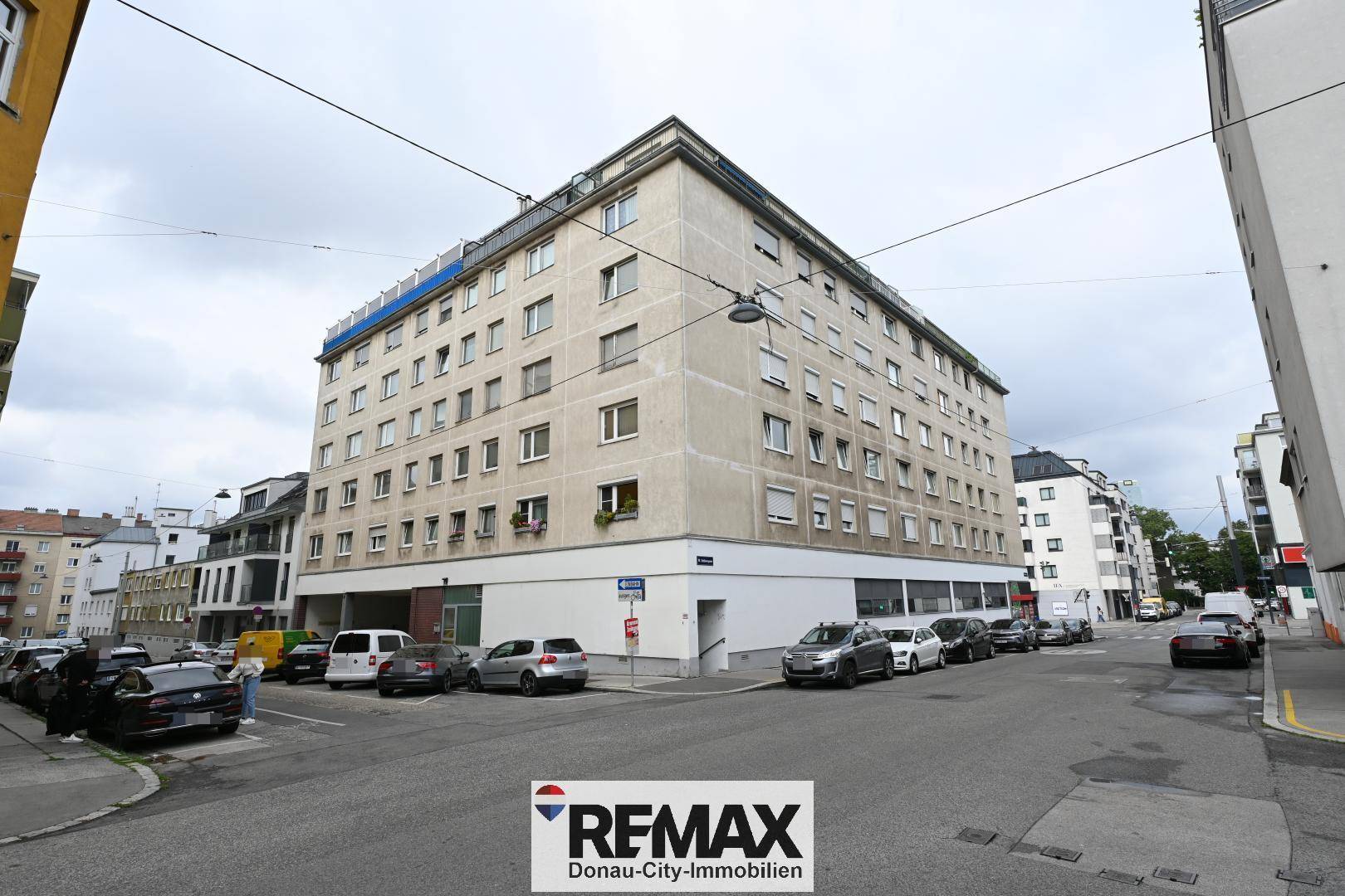 Mehrstöckiges Wohngebäude an einer Straßenecke mit parkenden Autos und urbaner Architektur.