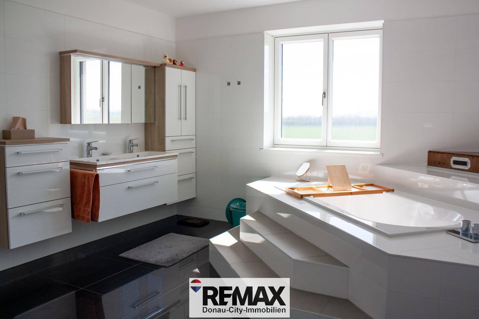 Modernes Badezimmer mit großer Eckbadewanne, Doppelwaschbecken und viel Tageslicht durch das Fenster.