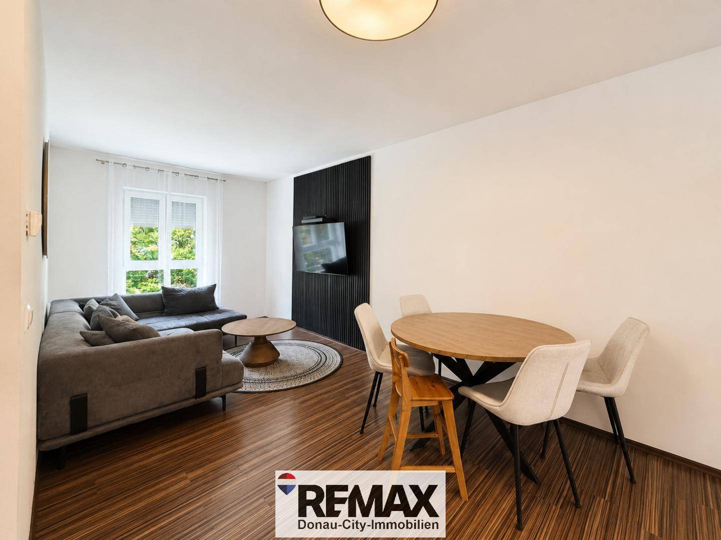 Helles Wohn- und Esszimmer mit Holzboden, bequemer Couch und modernem Esstisch.