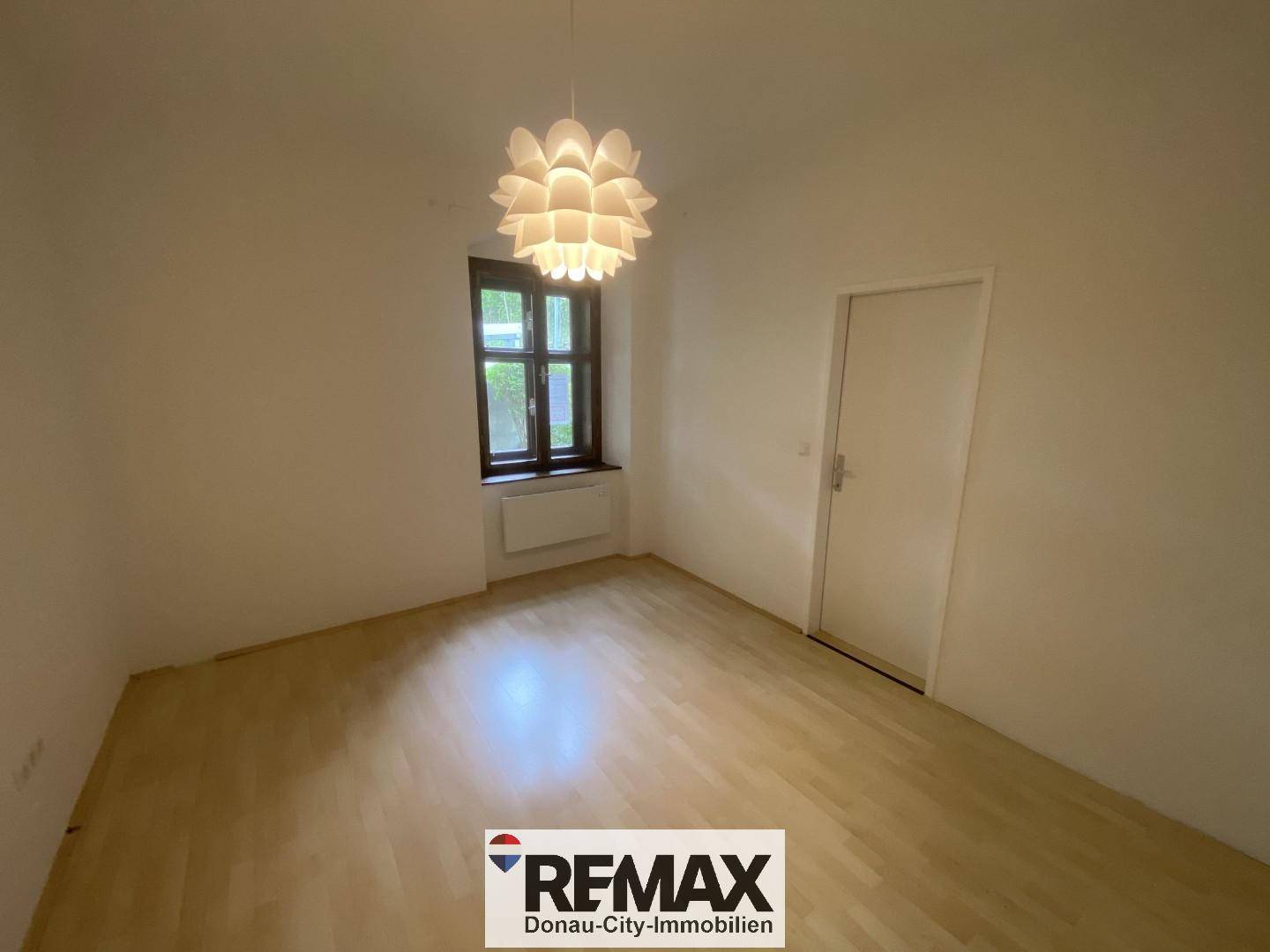 Helles Zimmer mit Parkettboden und dekorativer Deckenleuchte, ideal als Schlaf- oder Arbeitszimmer.