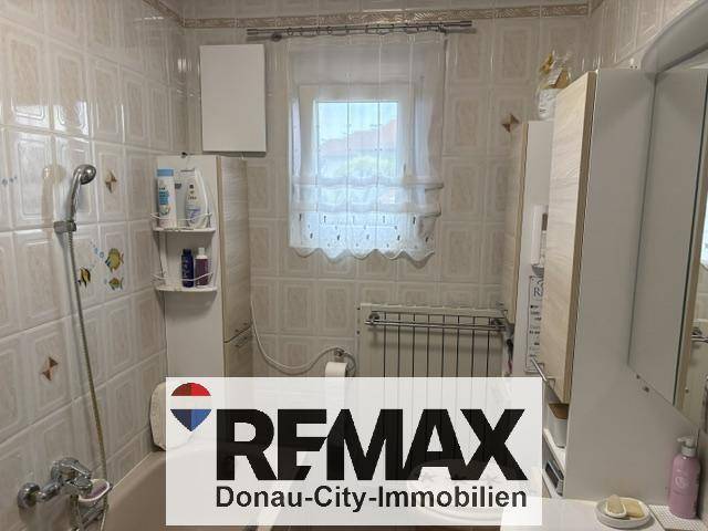 Badezimmer mit weißen Fliesen, Badewanne mit Duschfunktion und Fenster.