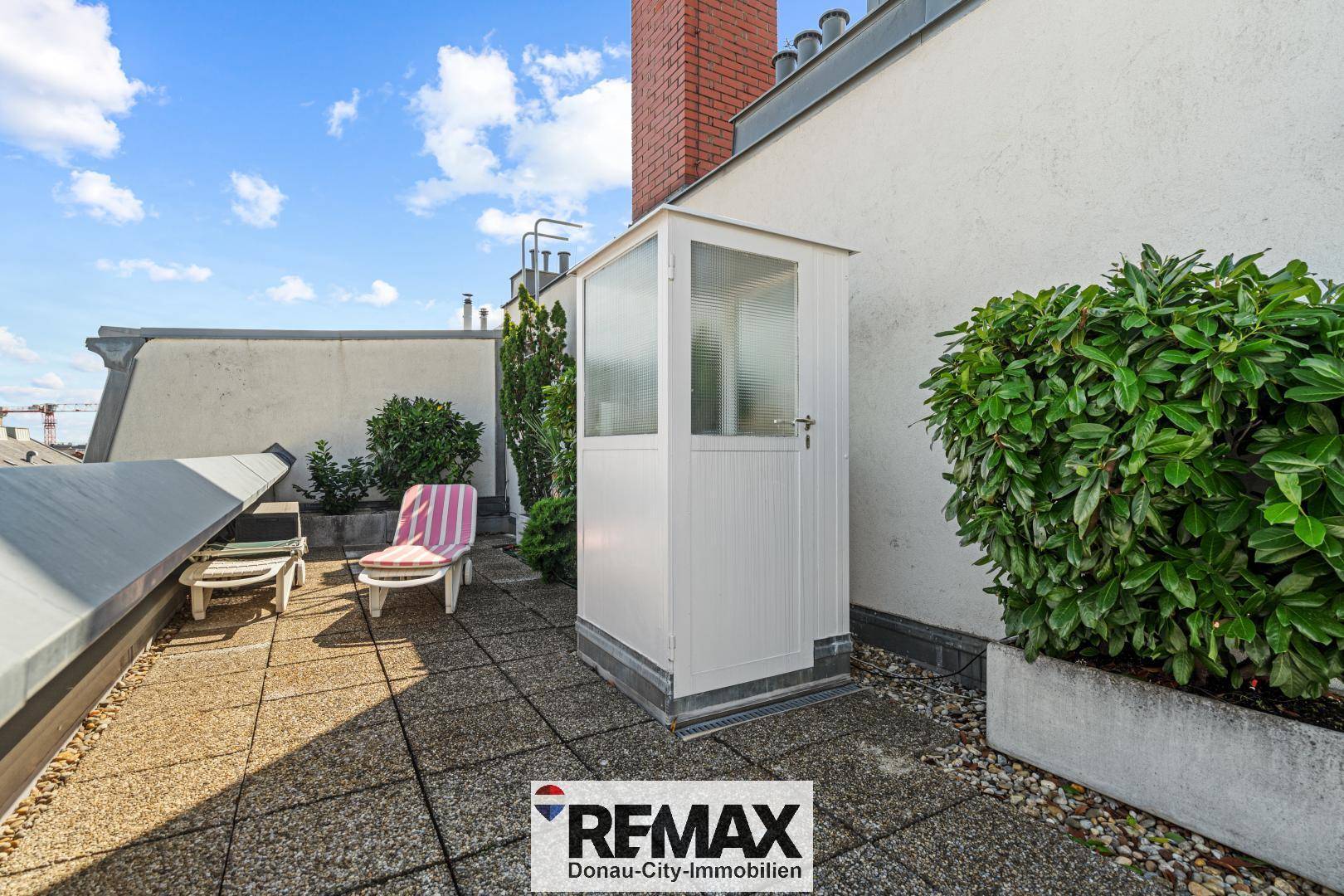 Dachterrasse mit Steinplattenboden, Liegestühlen und einem kleinen Gartenhaus.