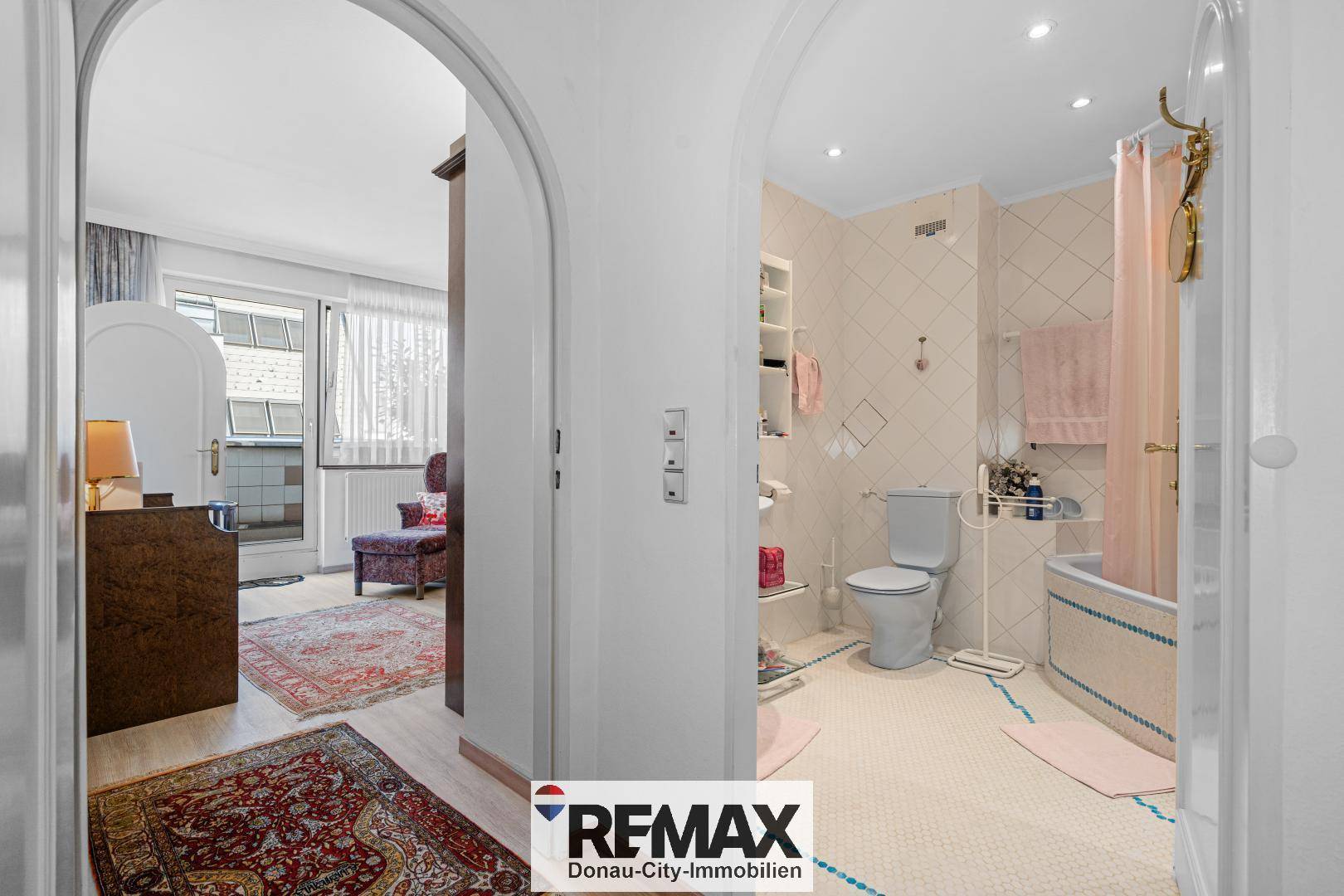 Badezimmer mit Badewanne, Toilette und Fliesenboden, verbunden mit einem weiteren Raum.