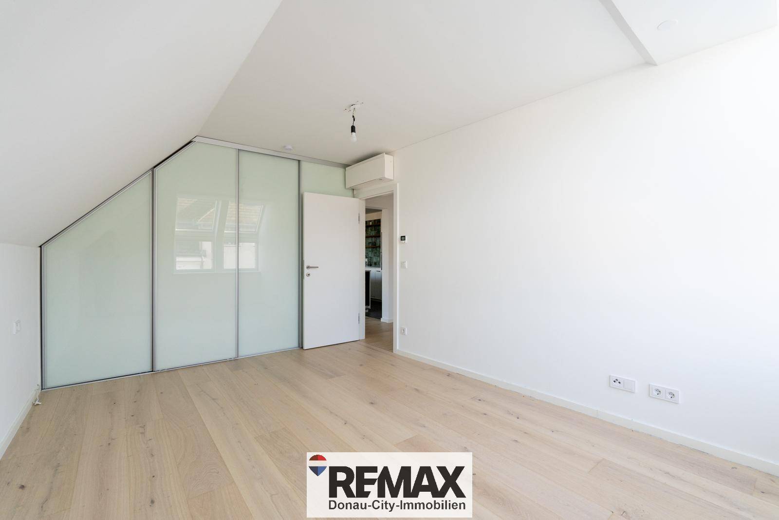 Schlafzimmer mit Dachschrägen, Einbauschrank und Zugang zu weiteren Räumen.
