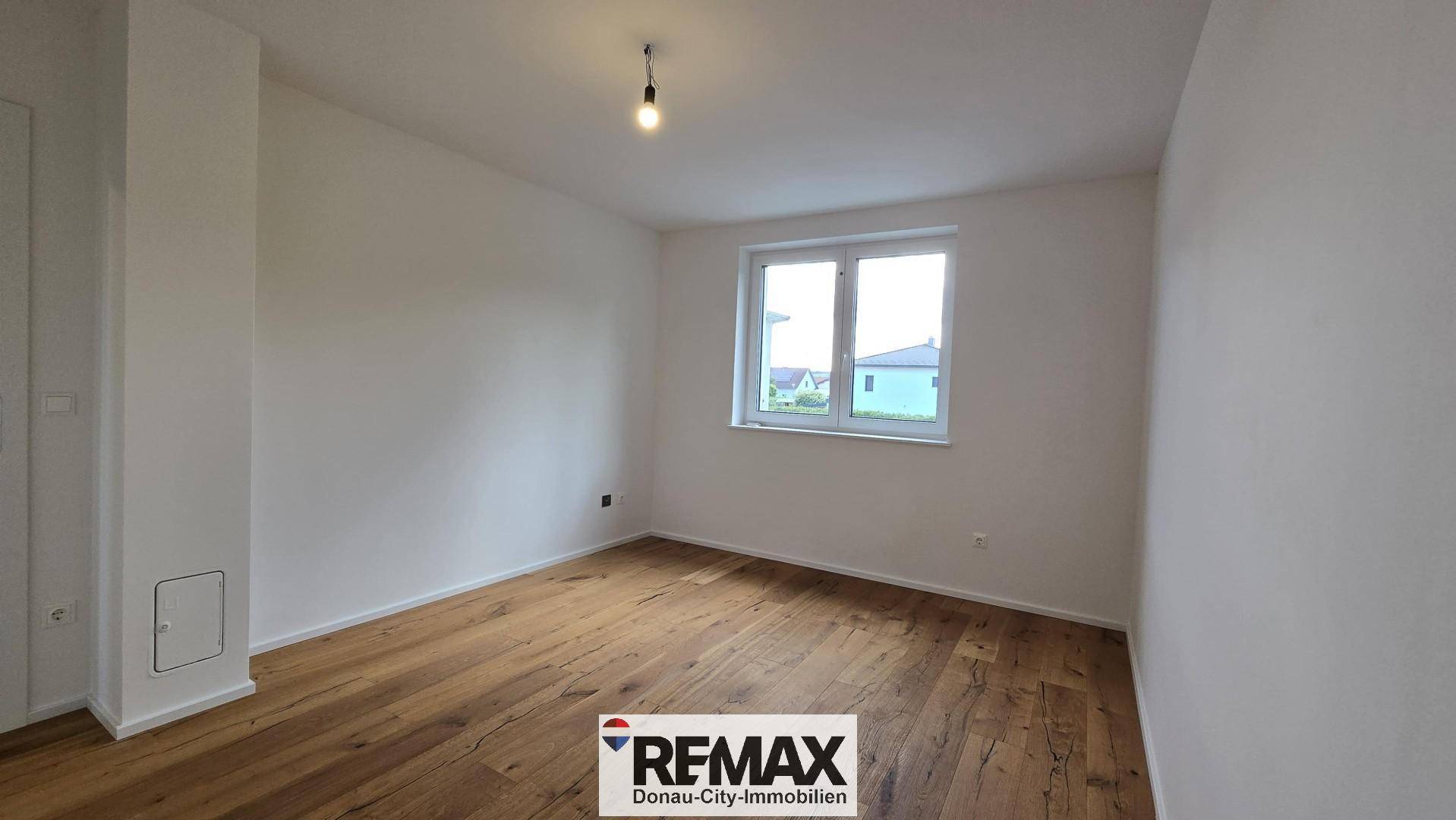 Schlafzimmer mit Holzparkett und Fenster, das viel Tageslicht in den Raum lässt.