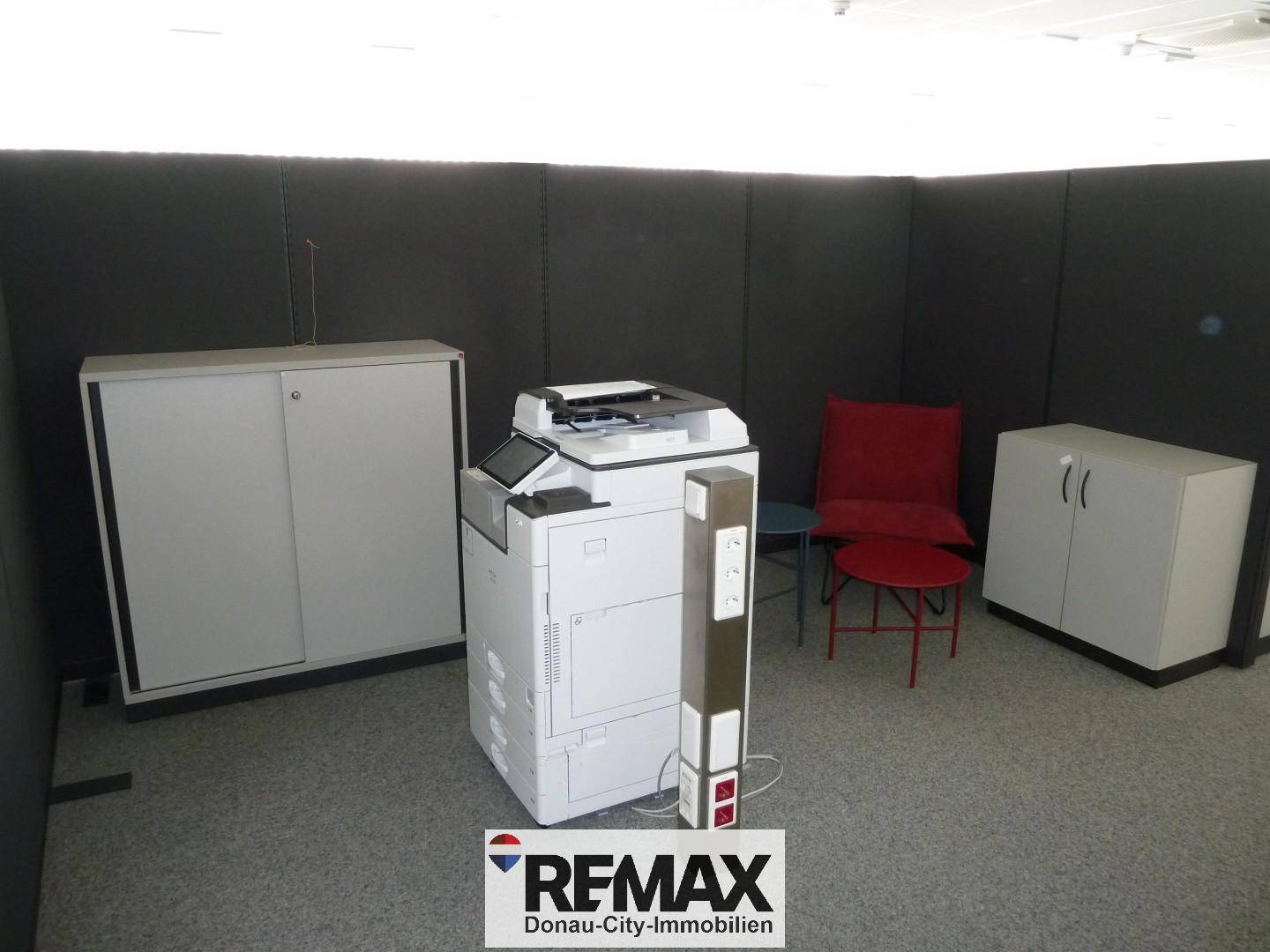 Bürobereich mit einem großen Multifunktionsdrucker, Aktenschränken und einem roten Sessel.