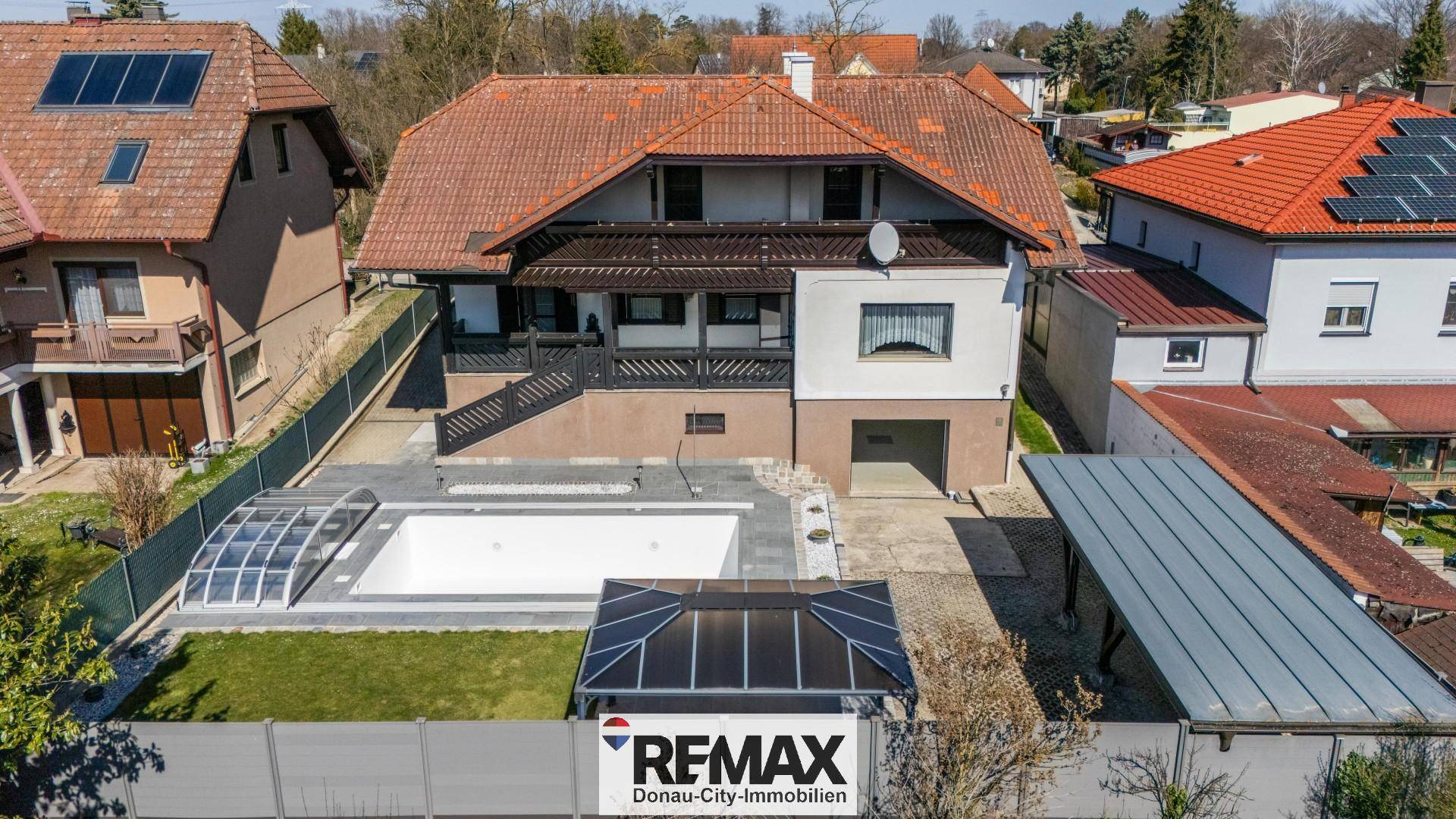 Luftaufnahme des Anwesens mit Haus, Pool und umliegender Wohngegend unter blauem Himmel.