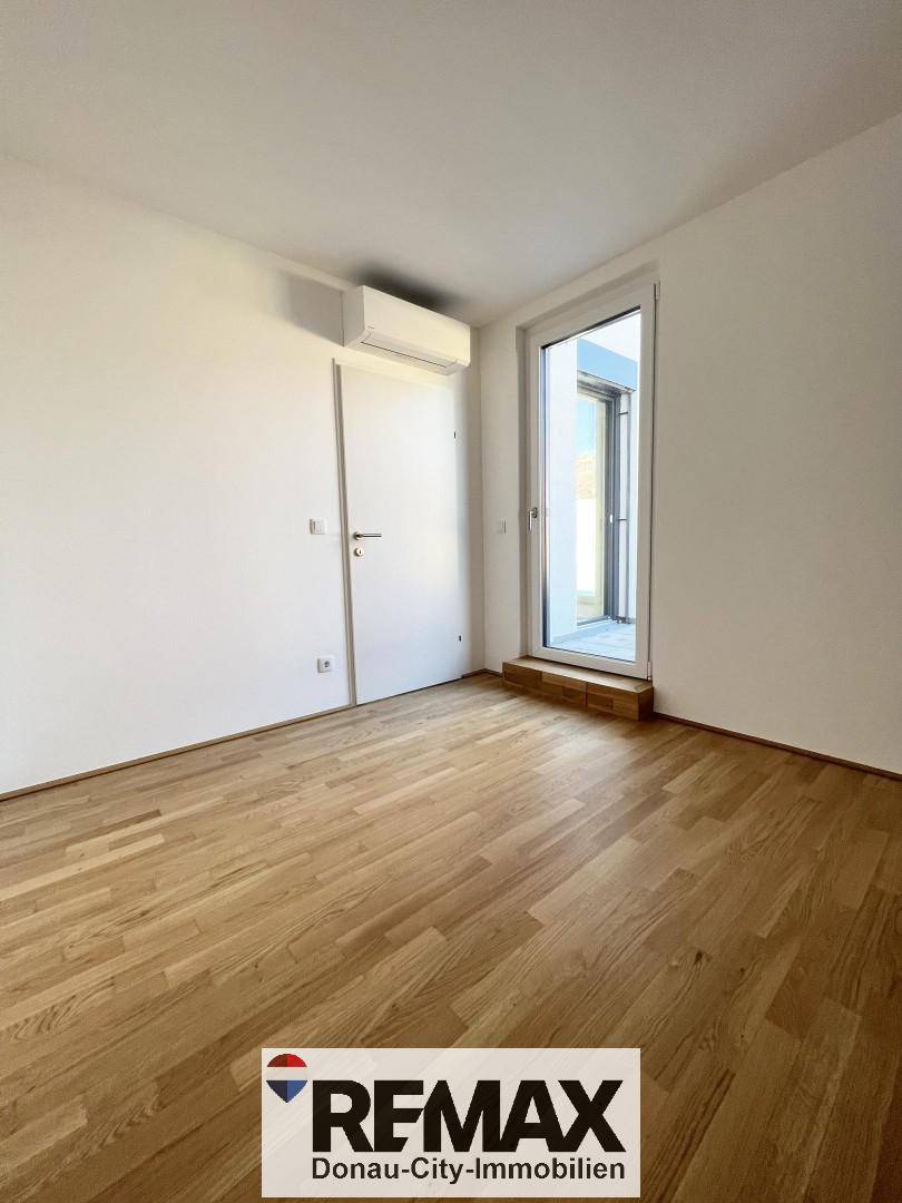 Leeres Zimmer mit hellem Parkettboden, weißen Wänden und Zugang zu einem Außenbereich.