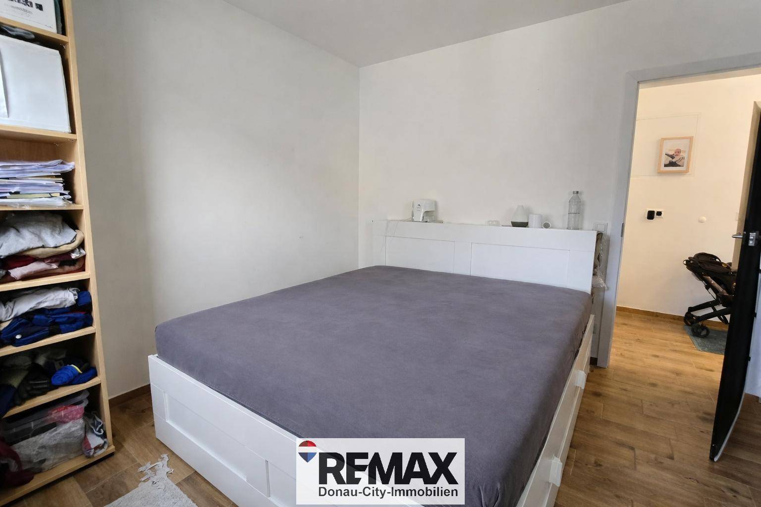 Helles Schlafzimmer mit weißem Bett, Holzboden und einem praktischen Bücherregal.