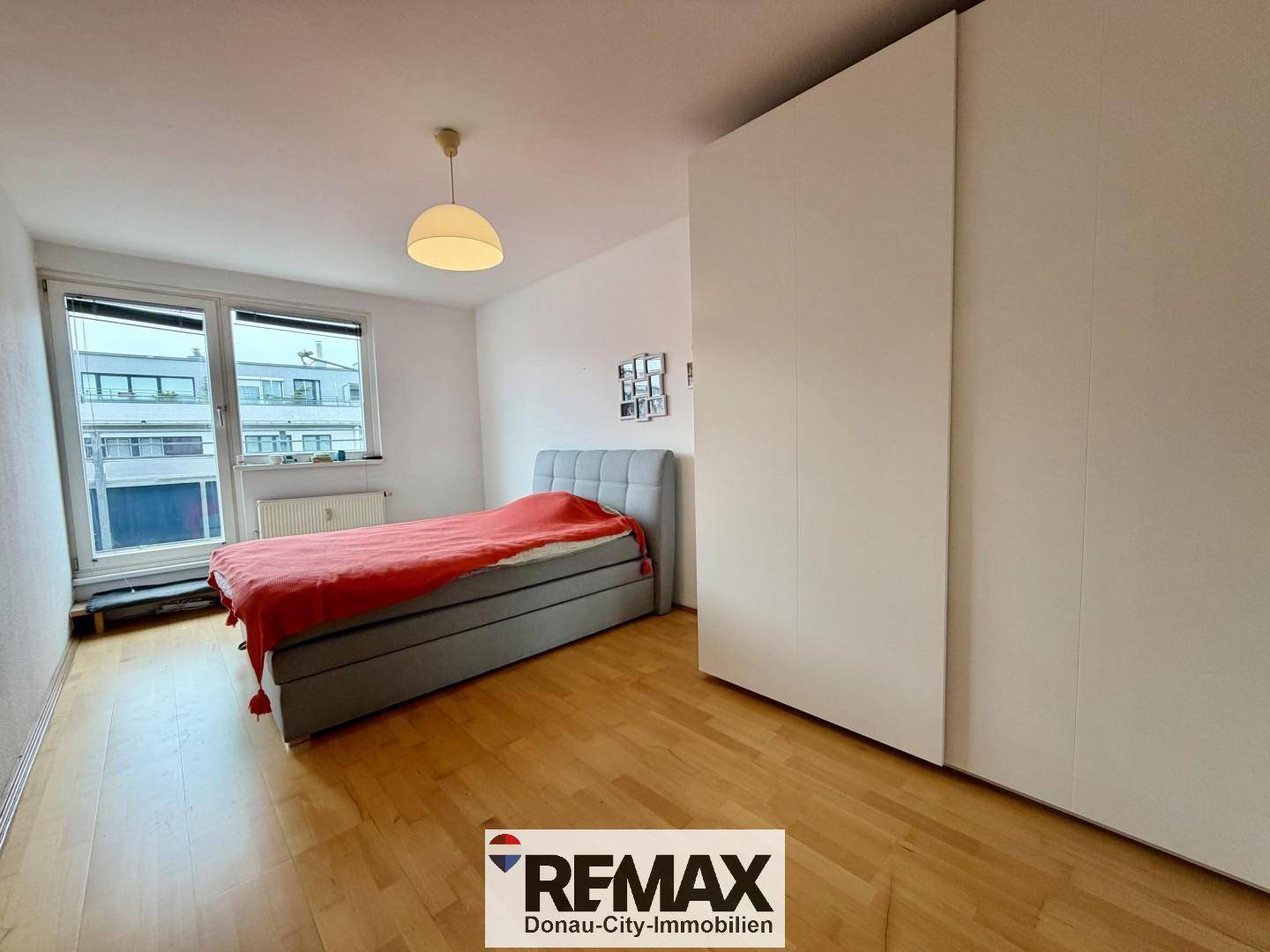 Schlafzimmer mit Holzboden, großem Kleiderschrank und Fenster mit Blick nach draußen.