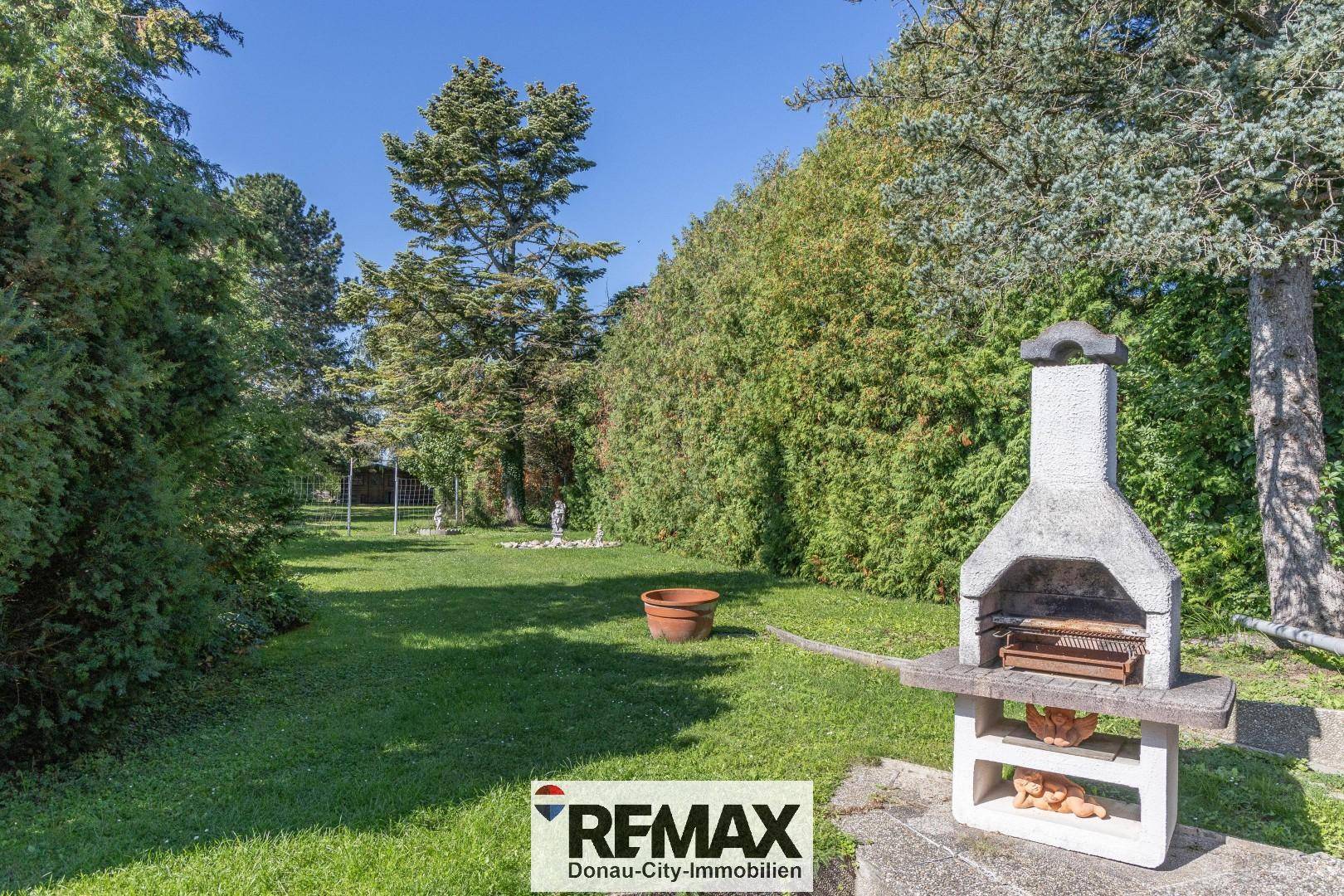 Großer Garten mit Rasenfläche, Bäumen und einem gemauerten Grillplatz für gesellige Abende.