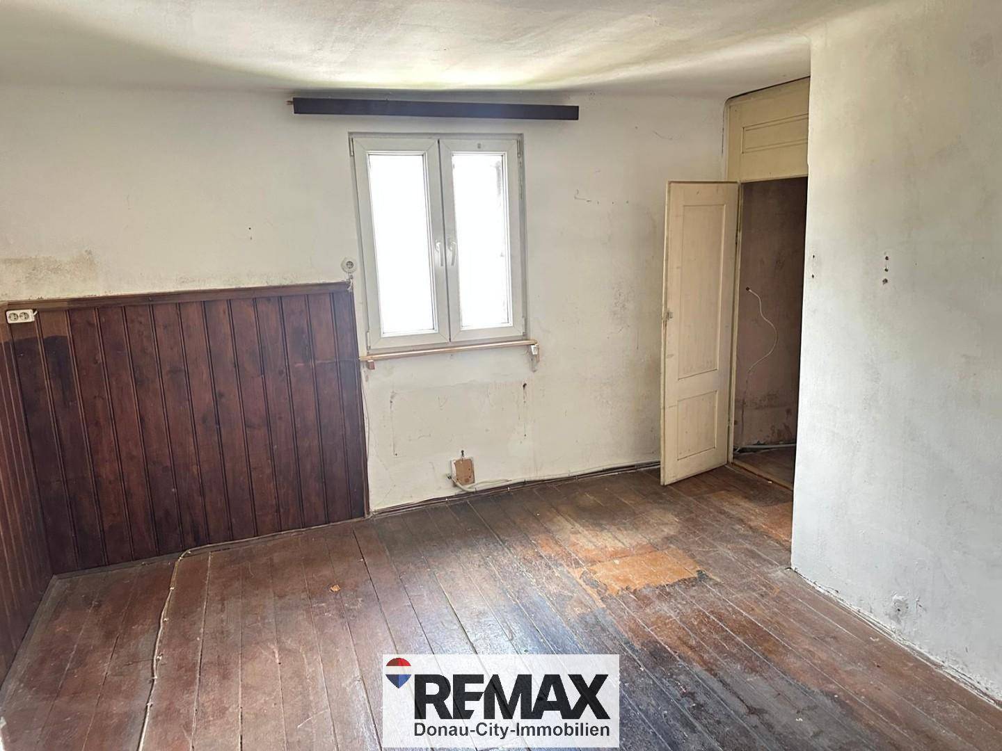 Leerer Raum mit Holzvertäfelung an einer Wand und abgenutztem Dielenboden.