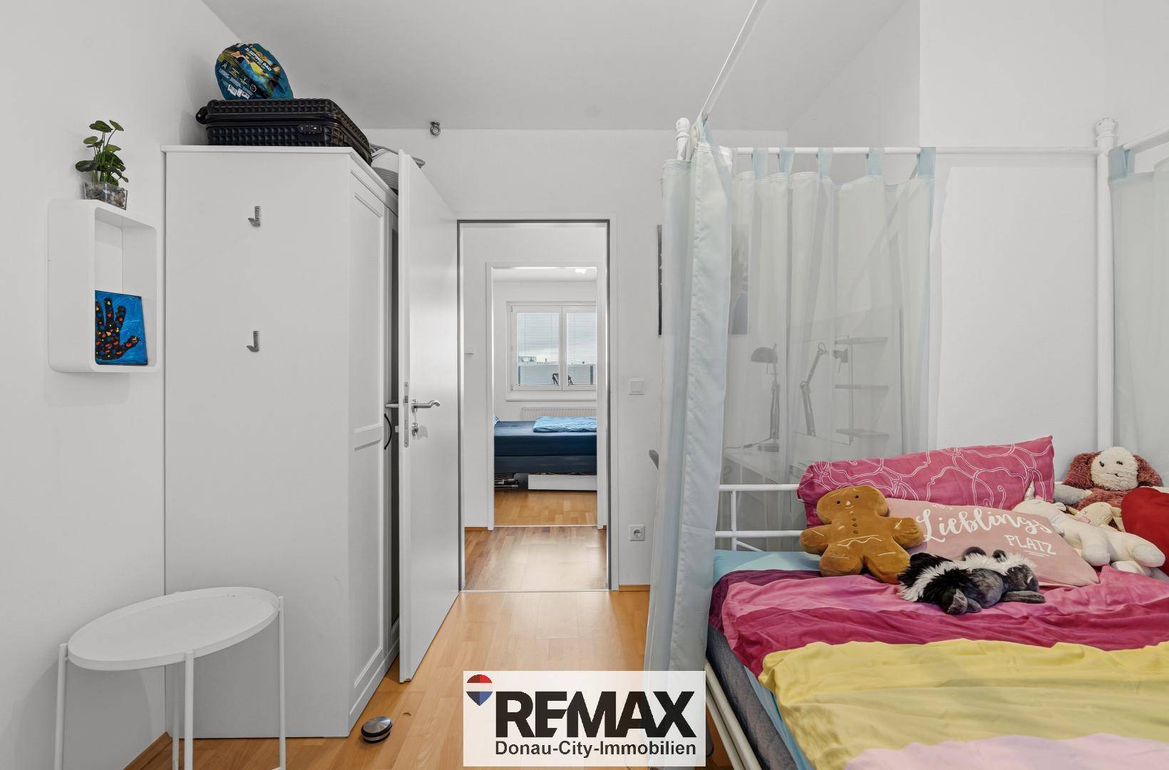 Helles Schlafzimmer mit Holzboden und Zugang zu einem weiteren Raum.