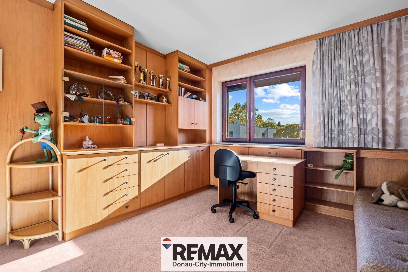 Gemütliches Arbeitszimmer mit maßgefertigten Holzregalen, Schreibtisch und Teppichboden.