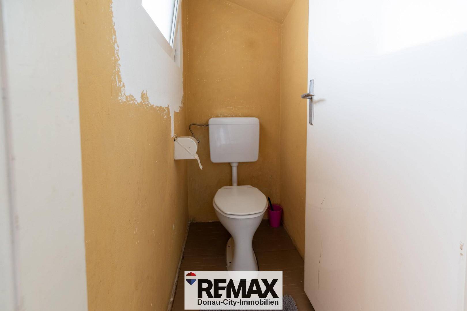 Separate Toilette mit WC und kleinem Fenster, Wände teilweise gestrichen.