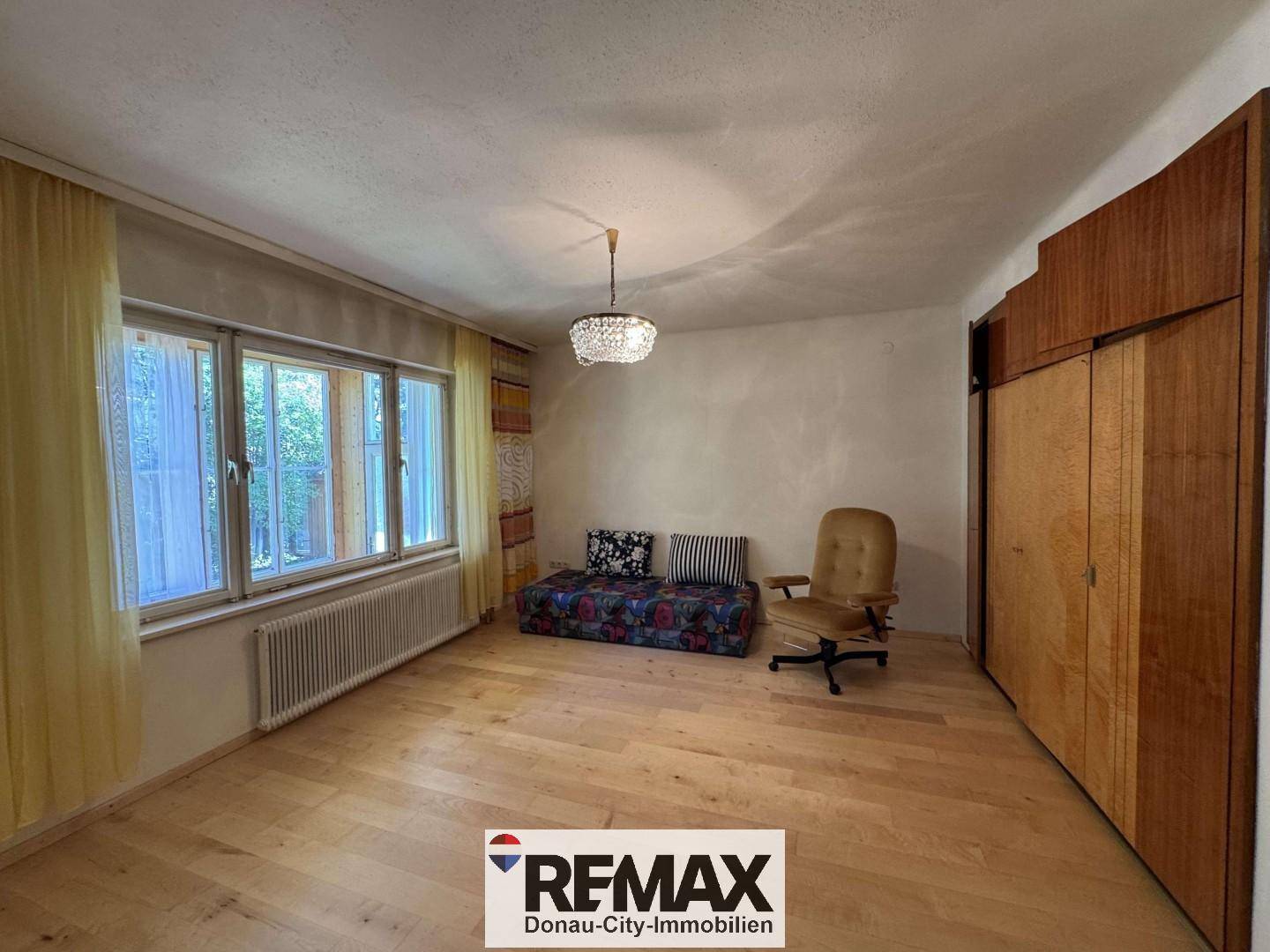 Helles Zimmer mit Holzfußboden, großen Fenstern und einem Kleiderschrank.