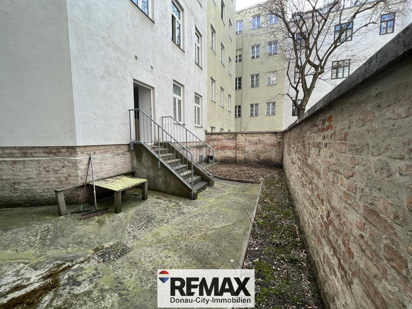 Hinterhofbereich mit Treppe zum Gebäude und einer alten Ziegelmauer.