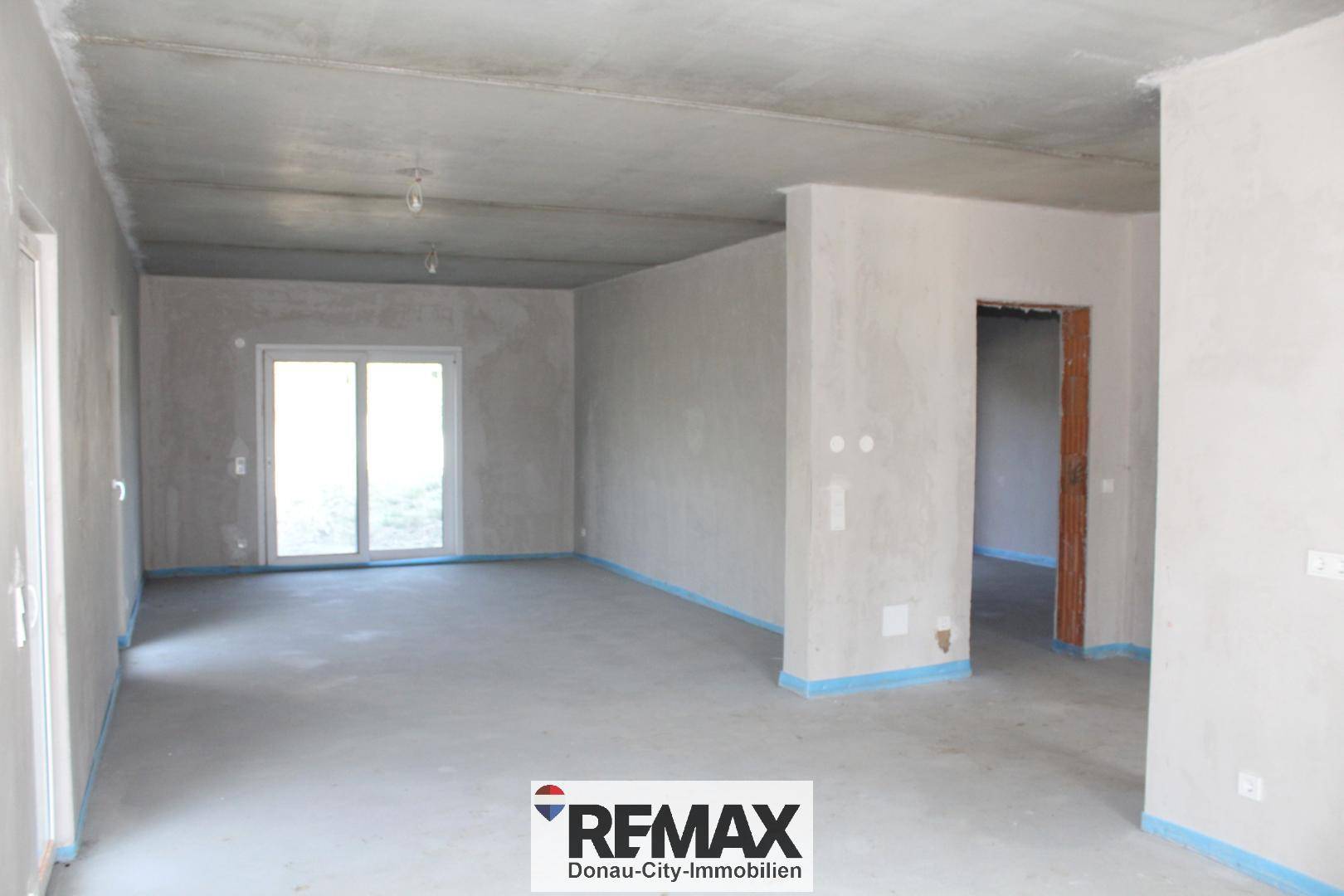 Geräumiger, unfertiger Innenraum mit Betonwänden und Schiebetür, bereit für den Ausbau.