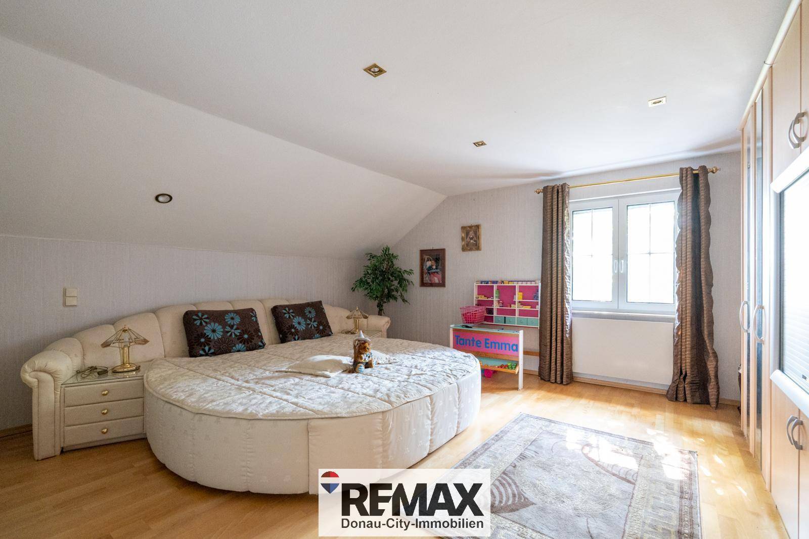 Gemütliches Schlafzimmer im Dachgeschoss mit rundem Bett, Holzboden und Einbauschränken.