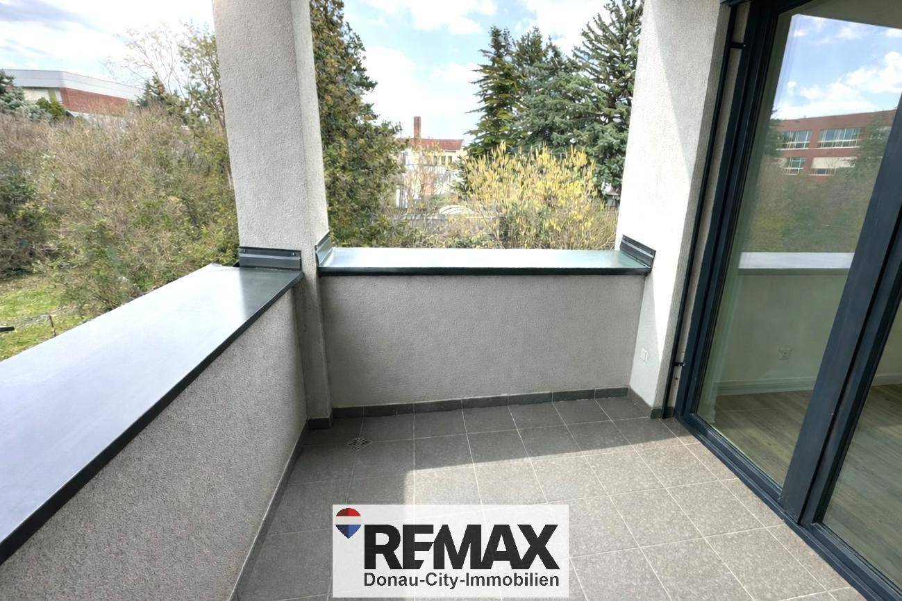 Balkon mit Fliesenboden und Blick auf Bäume sowie umliegende Gebäude.