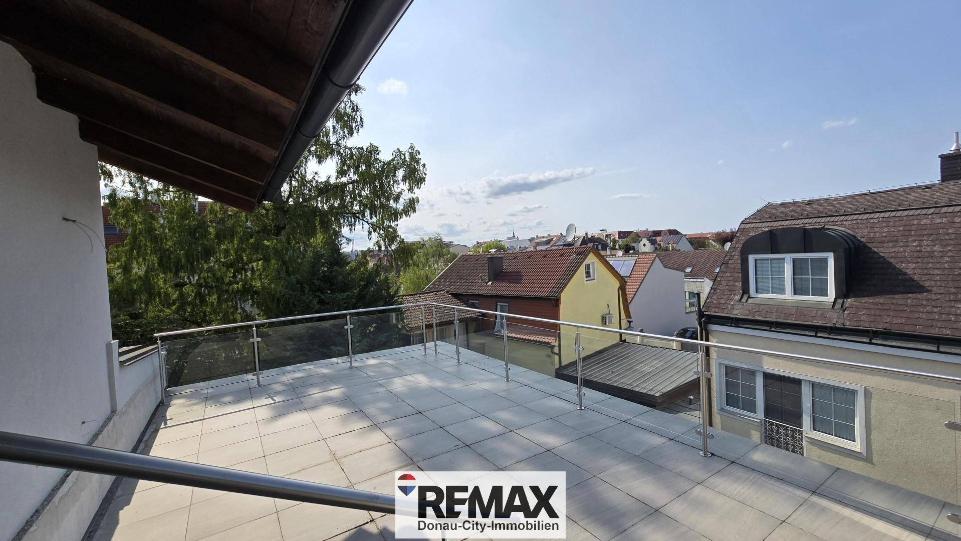 Großzügige Dachterrasse mit Fliesenboden und Glasgeländer, bietet einen weiten Blick über die Dächer.