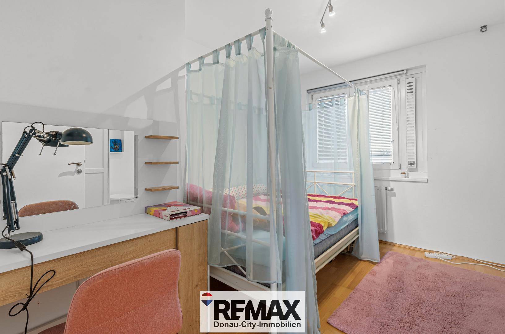 Kinderzimmer mit Himmelbett, Schreibtisch und rosa Teppichboden.