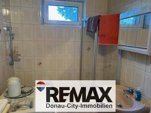 Badezimmer mit gefliesten Wänden, Waschbecken, Duschkabine und Fenster.