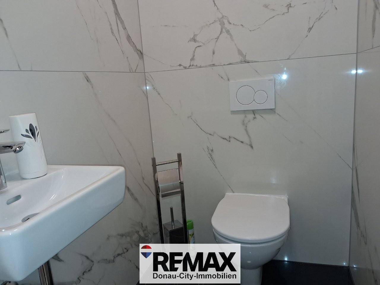 Helles Gäste-WC mit Marmorfliesen, wandmontierter Toilette und kleinem Waschbecken.