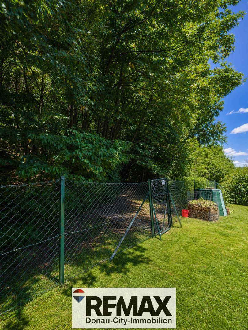 Gepflegter Gartenbereich mit Zaun, Kompostbehältern und altem Baumbestand im Hintergrund.