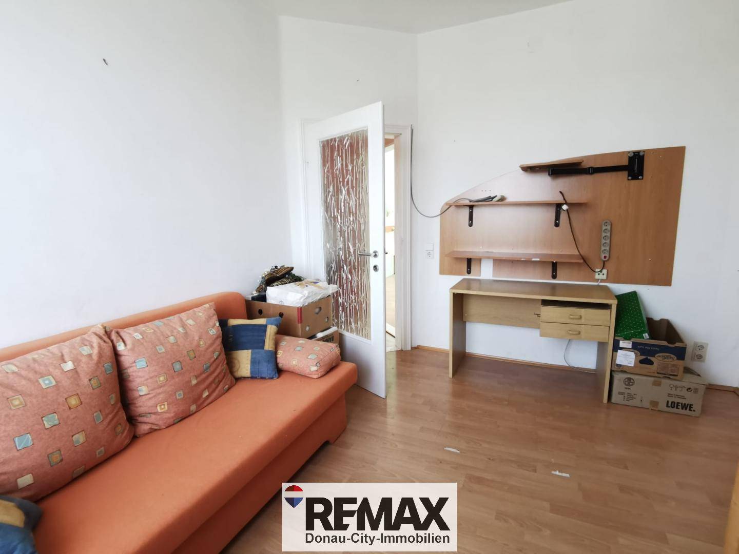 Heller Raum mit orangefarbenem Sofa, Laminatboden und weiß gestrichenen Wänden.