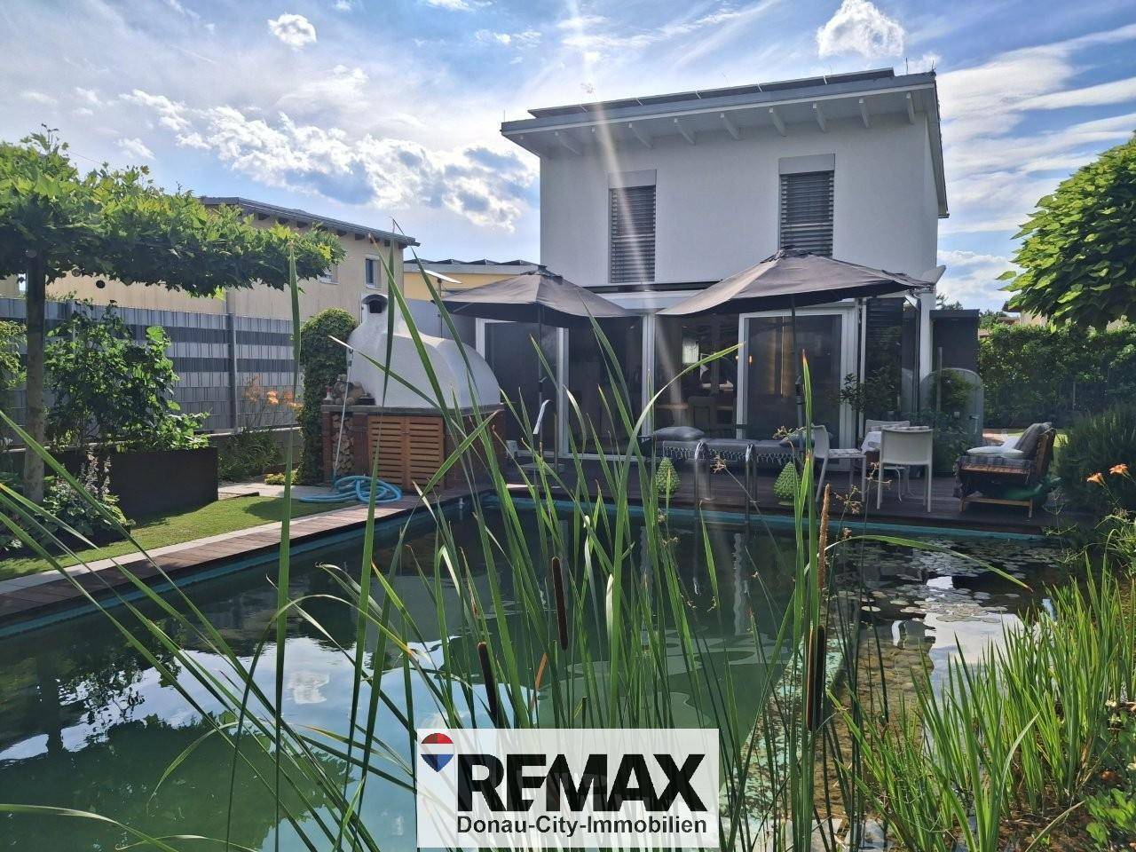 Rückseite des Hauses mit großer Terrasse, Sonnenschirmen und Blick auf den Schwimmteich.
