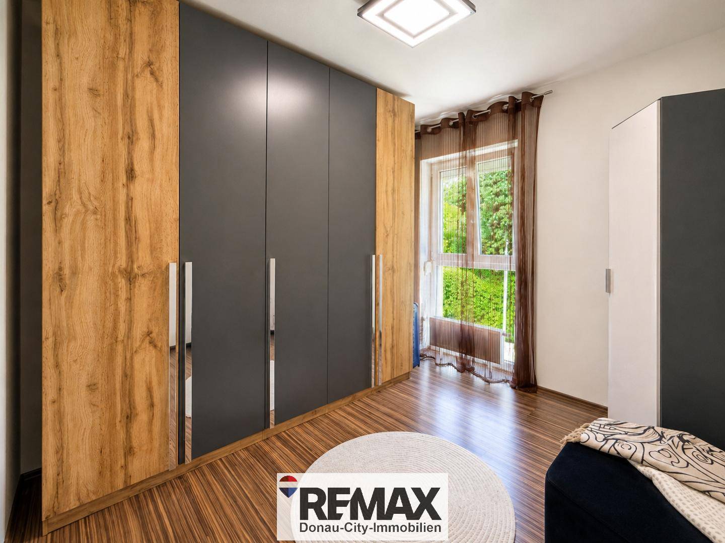 Schlafzimmer mit großem Einbauschrank in Holz- und Anthrazitoptik und Fenster.