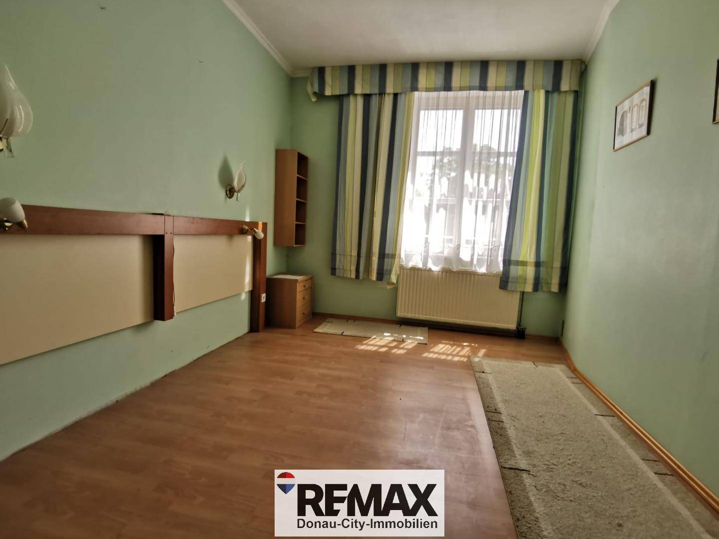 Schlafzimmer mit grünen Wänden, Laminatboden und Fenster mit Heizkörper.