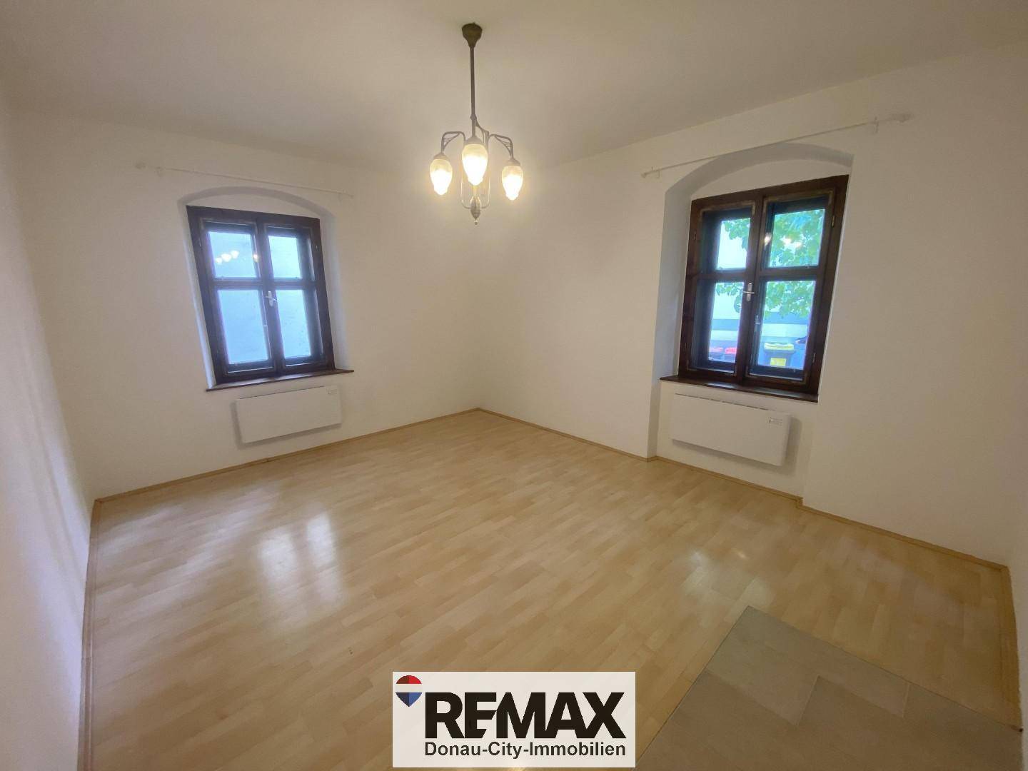 Helles, leeres Zimmer mit Parkettboden und zwei Fenstern, bereit zur individuellen Gestaltung.