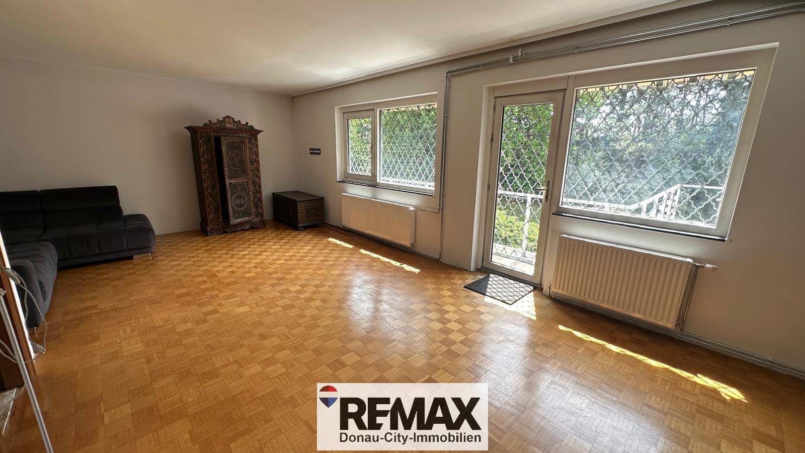 Wohnzimmer mit Parkettboden, großen Fenstern und Zugang zu einem französischen Balkon.