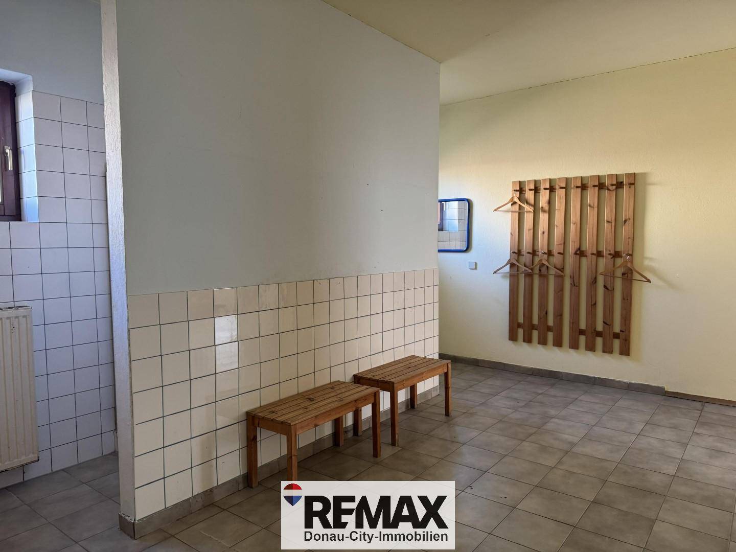 Umkleideraum mit gefliesten Wänden, Holzbänken und einer Garderobe, ideal für Sport- oder Freizeitaktivitäten.