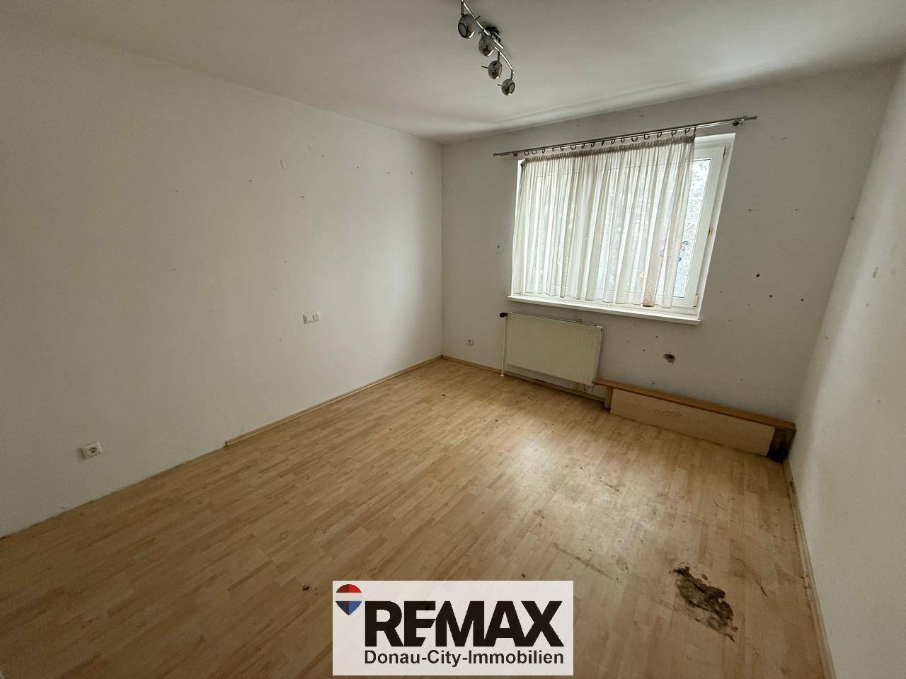 Leeres Schlafzimmer mit Laminatboden und einem Fenster, das viel Tageslicht hereinlässt.