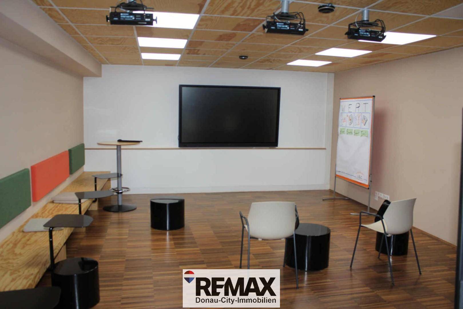 Präsentationsraum mit großer Leinwand, integrierter Sitzbank und flexiblen Möbeln für Veranstaltungen.